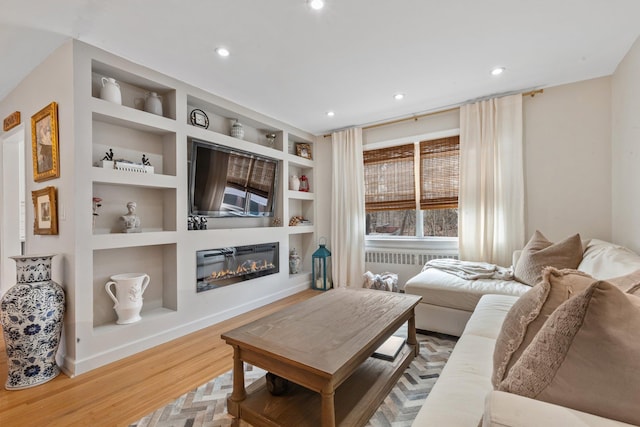 living room featuring built in features, wood finished floors, baseboards, recessed lighting, and a glass covered fireplace