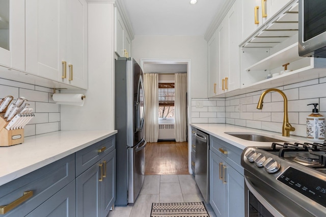 kitchen with appliances with stainless steel finishes, white cabinetry, radiator heating unit, and a sink