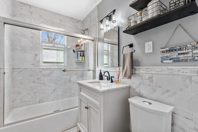 bathroom featuring vanity, tile walls, toilet, and enclosed tub / shower combo