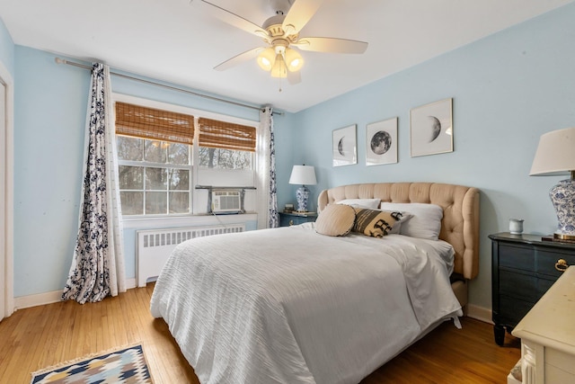 bedroom with cooling unit, radiator heating unit, baseboards, and wood finished floors