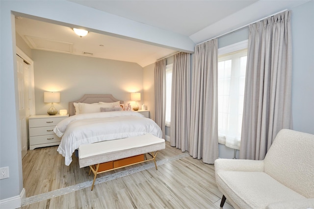 bedroom featuring lofted ceiling, light wood-style floors, attic access, and visible vents