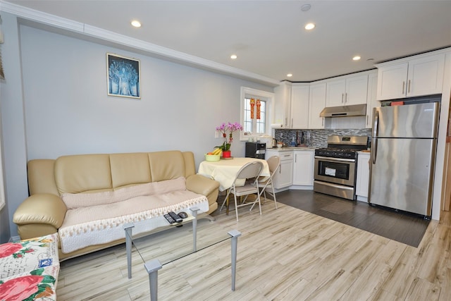 kitchen with white cabinets, decorative backsplash, wood finished floors, stainless steel appliances, and under cabinet range hood