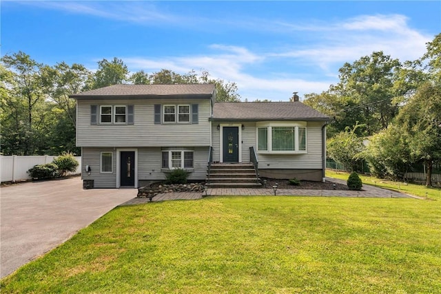 split level home with a chimney, fence, and a front lawn