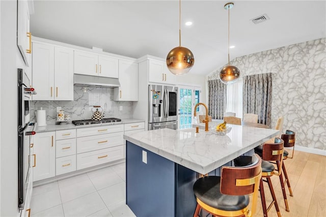 kitchen featuring a breakfast bar, stainless steel appliances, visible vents, white cabinetry, and under cabinet range hood