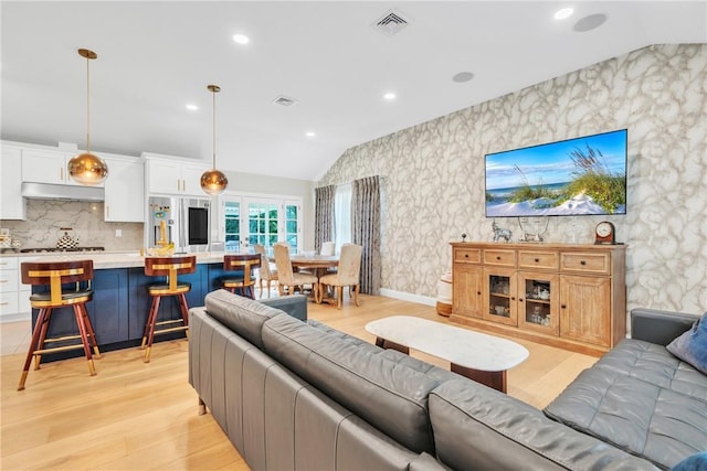 living area featuring vaulted ceiling, light wood-style floors, visible vents, and wallpapered walls