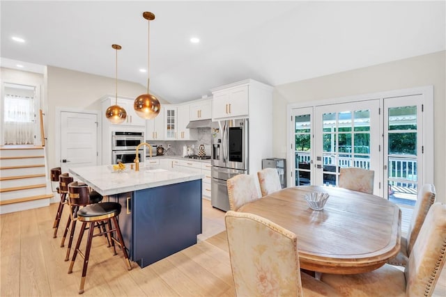 kitchen featuring a center island with sink, lofted ceiling, appliances with stainless steel finishes, white cabinetry, and backsplash