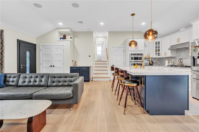 kitchen featuring visible vents, glass insert cabinets, white cabinetry, under cabinet range hood, and a kitchen breakfast bar