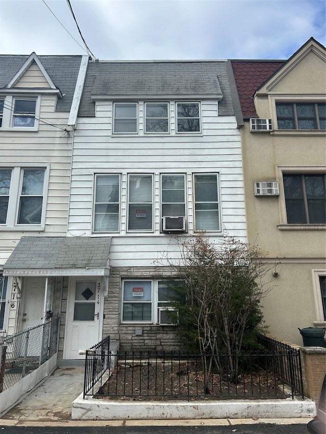 townhome / multi-family property with stone siding, a fenced front yard, cooling unit, and a shingled roof