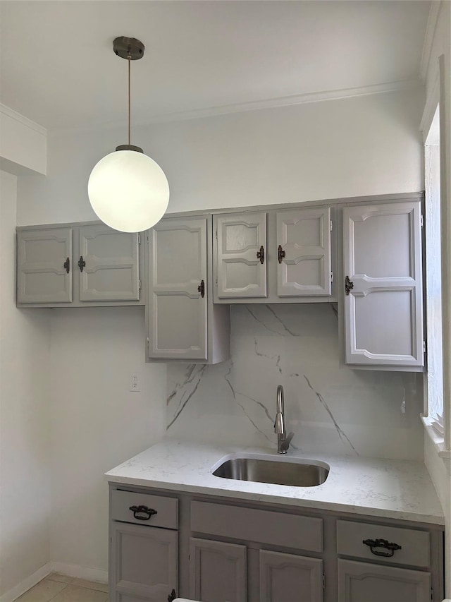 kitchen featuring crown molding, decorative backsplash, gray cabinets, and a sink