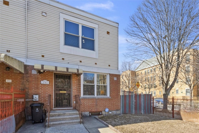 view of front of home with brick siding, entry steps, and fence