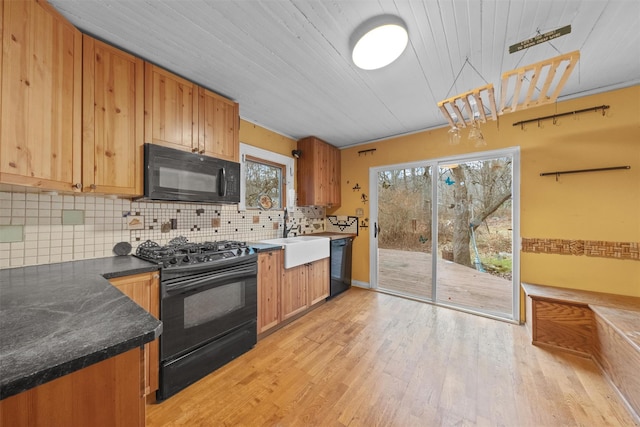 kitchen with black appliances, light wood-style flooring, a sink, dark countertops, and backsplash