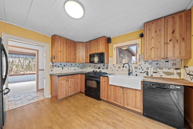 kitchen with light wood-type flooring, black appliances, light brown cabinets, a sink, and backsplash