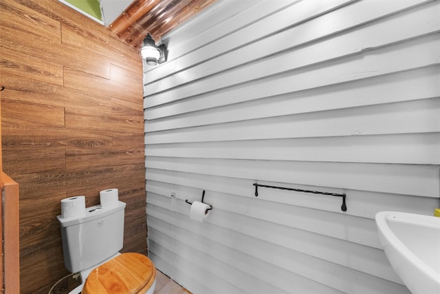 bathroom featuring wooden walls, toilet, and a sink