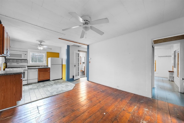 kitchen featuring white appliances, brown cabinetry, a sink, wood-type flooring, and dark countertops