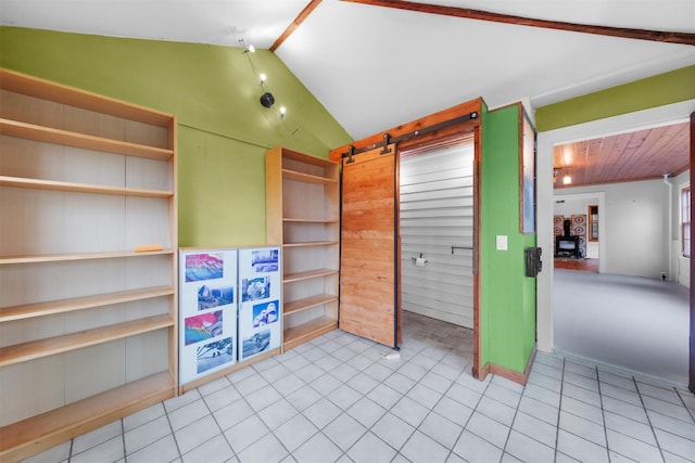 unfurnished bedroom with a barn door, wooden walls, and vaulted ceiling