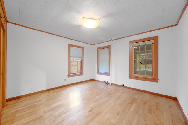 spare room with ornamental molding, light wood-style flooring, and baseboards