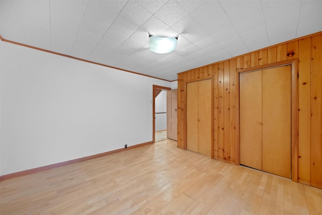 unfurnished bedroom with wood walls, crown molding, wood finished floors, and baseboards