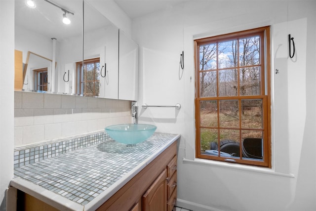 bathroom featuring rail lighting, vanity, baseboards, and backsplash