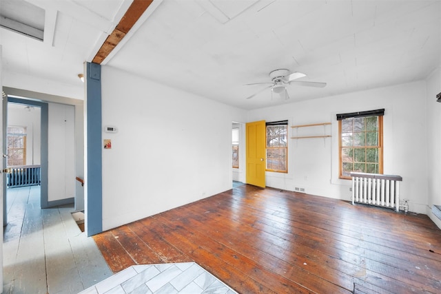 spare room featuring wood-type flooring, a ceiling fan, visible vents, and radiator heating unit