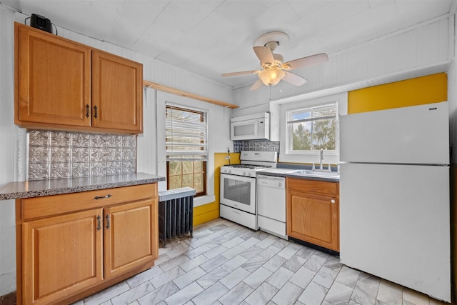 kitchen featuring a ceiling fan, a sink, brown cabinetry, decorative backsplash, and white appliances
