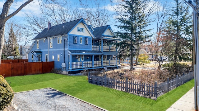 rear view of house featuring a chimney, roof with shingles, fence private yard, covered porch, and a yard