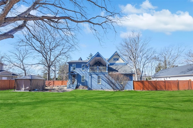 rear view of house with a balcony, a fenced backyard, a lawn, and a patio