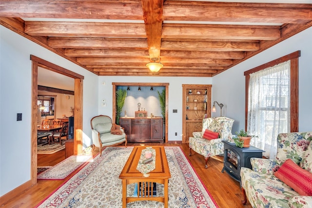 living area with baseboards, beamed ceiling, and wood finished floors