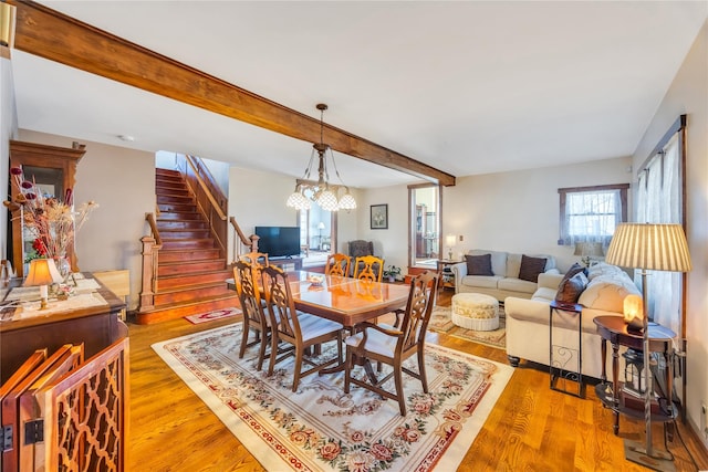 dining room with stairs, an inviting chandelier, beam ceiling, and light wood-style floors