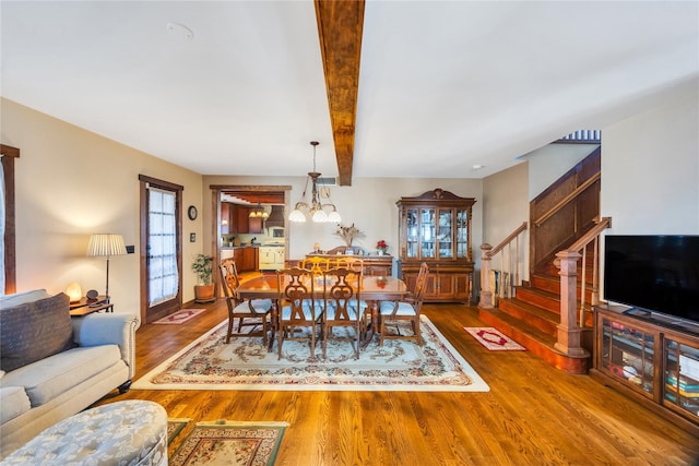 dining space featuring beamed ceiling, stairway, wood finished floors, and an inviting chandelier