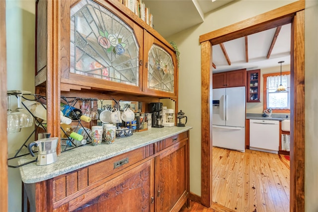 kitchen featuring brown cabinets, hanging light fixtures, light wood-style floors, glass insert cabinets, and white appliances