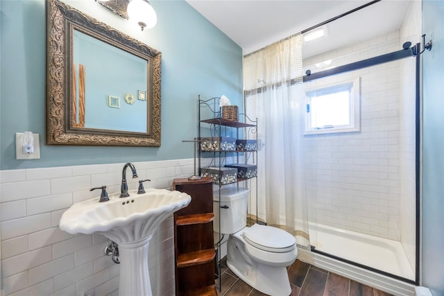 bathroom featuring wood finish floors, a wainscoted wall, tile walls, toilet, and a stall shower