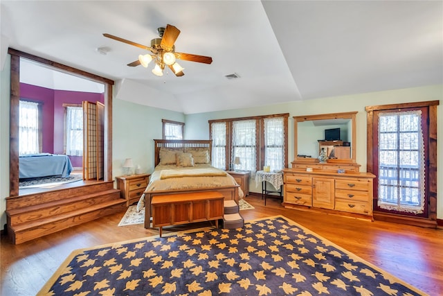 bedroom with lofted ceiling, multiple windows, visible vents, and wood finished floors