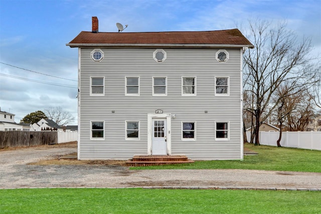 rear view of house with a chimney, fence, and a yard