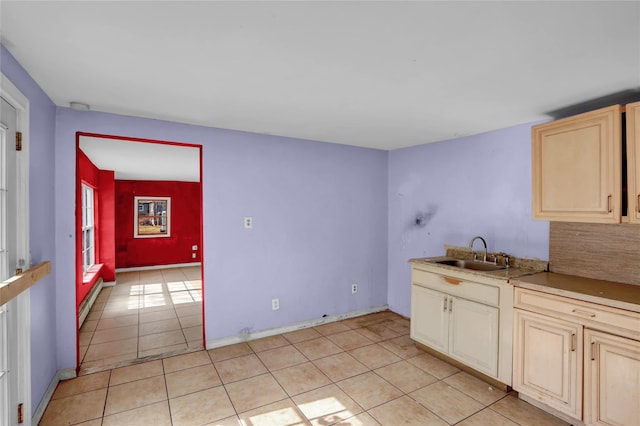 kitchen with light tile patterned floors, baseboard heating, light brown cabinets, a sink, and baseboards