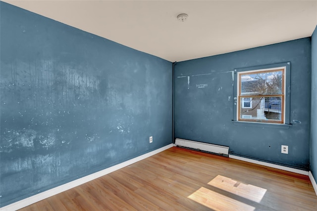 spare room with baseboards, a baseboard heating unit, and wood finished floors