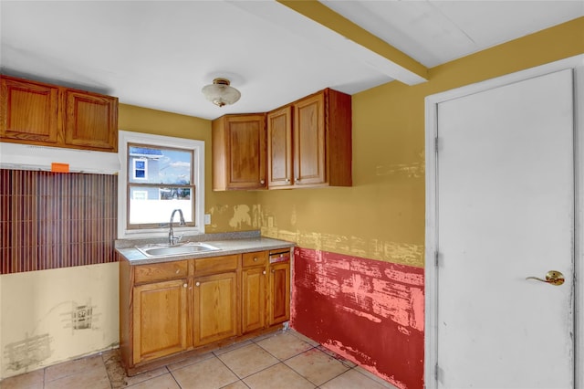 kitchen featuring light countertops, brown cabinetry, a sink, and beam ceiling