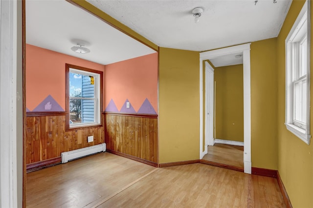 empty room with beam ceiling, a baseboard radiator, wainscoting, wood walls, and wood finished floors