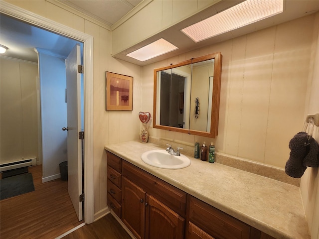 bathroom with a decorative wall, wood finished floors, vanity, baseboard heating, and crown molding