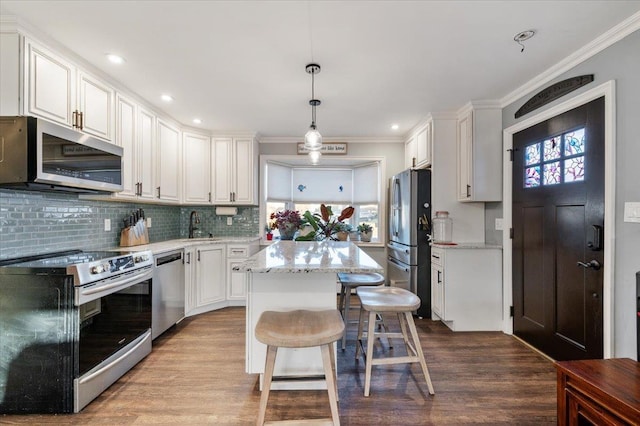 kitchen featuring a kitchen island, ornamental molding, appliances with stainless steel finishes, white cabinetry, and dark wood-style flooring