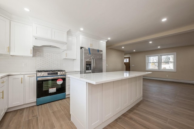 kitchen with light wood-style flooring, a baseboard heating unit, stainless steel appliances, white cabinets, and decorative backsplash