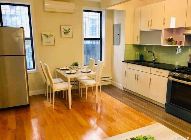 kitchen with wood finished floors, a sink, appliances with stainless steel finishes, a wall mounted AC, and electric panel