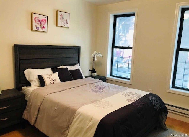 bedroom with a baseboard heating unit and wood finished floors