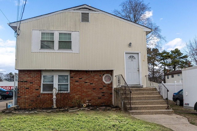 view of front of property featuring brick siding, a front lawn, and fence