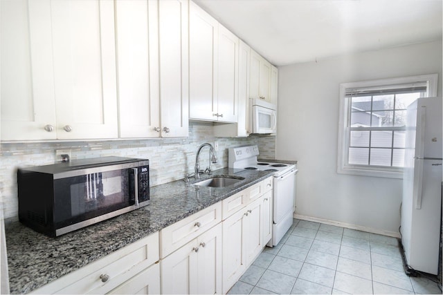 kitchen featuring white appliances, a sink, white cabinets, backsplash, and dark stone counters