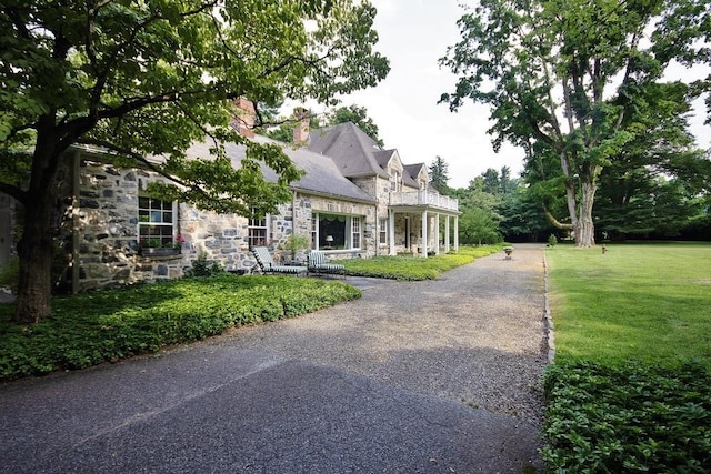 view of front of home featuring a front yard, stone siding, driveway, and a chimney