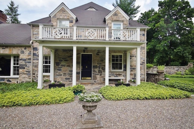 view of front facade with a balcony, covered porch, and stone siding