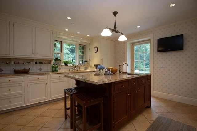 kitchen with ornamental molding, white cabinets, a sink, plenty of natural light, and wallpapered walls