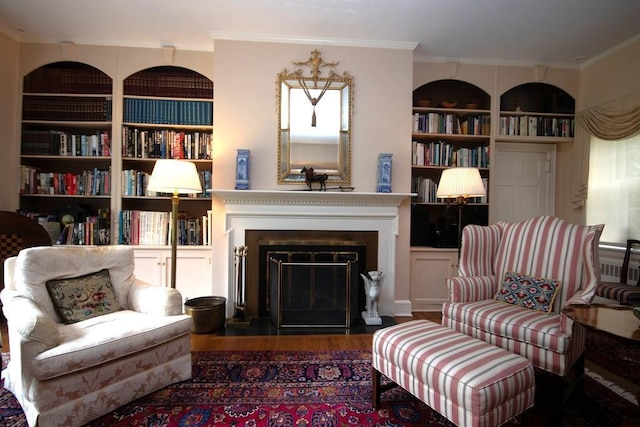 living area with a fireplace with flush hearth, built in shelves, wood finished floors, and crown molding