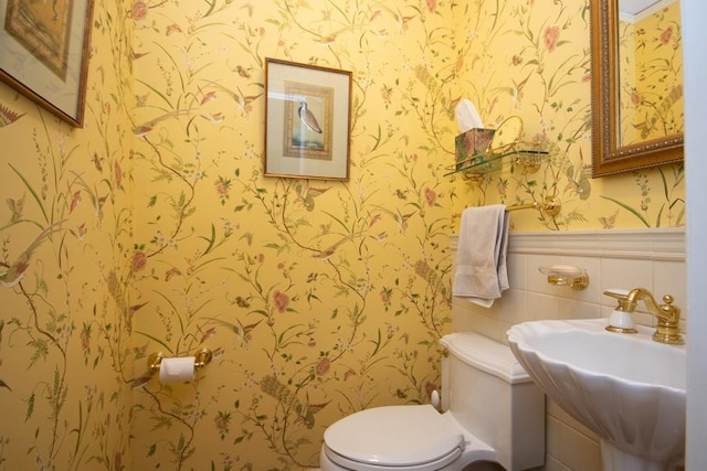 bathroom with a wainscoted wall, a sink, toilet, and wallpapered walls