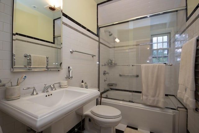 full bath featuring tile walls, decorative backsplash, toilet, combined bath / shower with glass door, and a sink